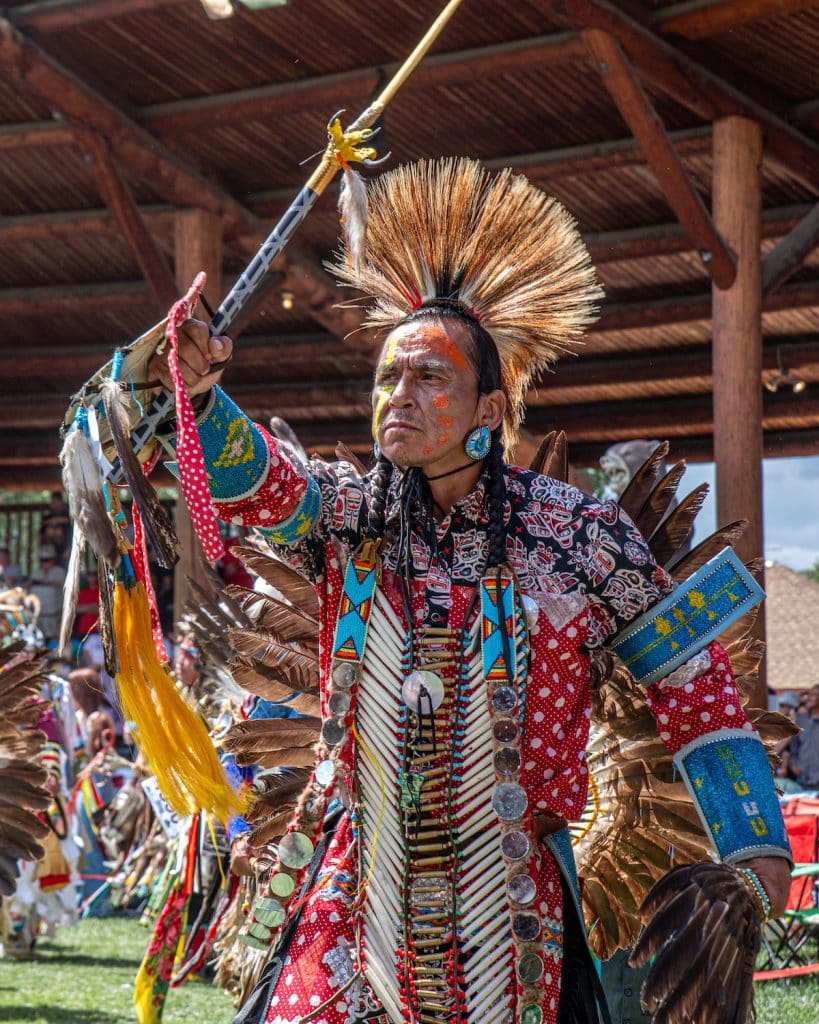 A dancer performs at Kamloopa powwow 2025 wearing a feathered crown and bright blue and red colours 