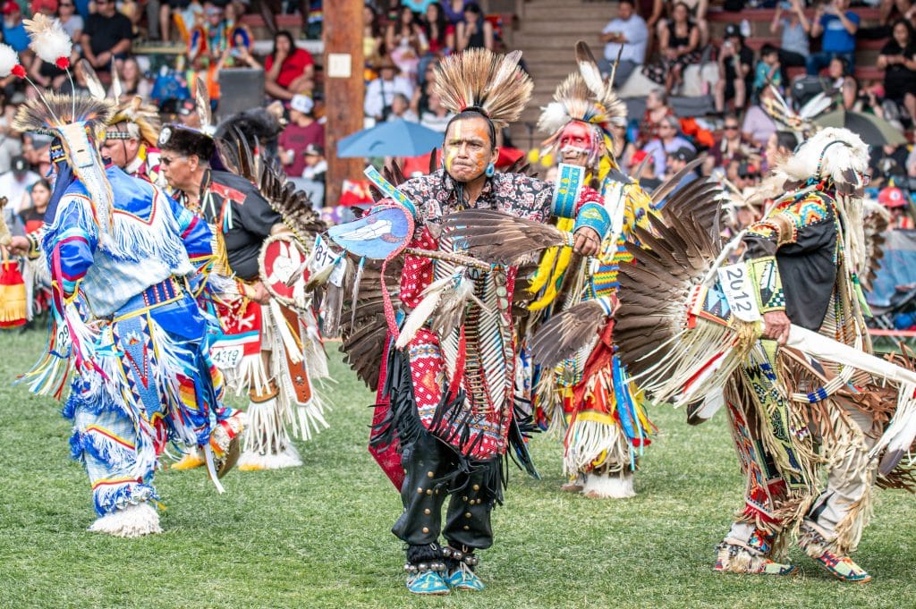 A dancer at 2025 Kamloopa powwow wears a grass head dress and regalia dancing in a crowd of people at the arbour.