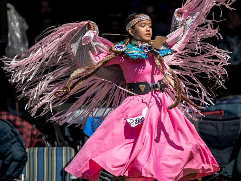 A young dancer raises her arms wearing pink regalia at 2025 Kamloopa powwow