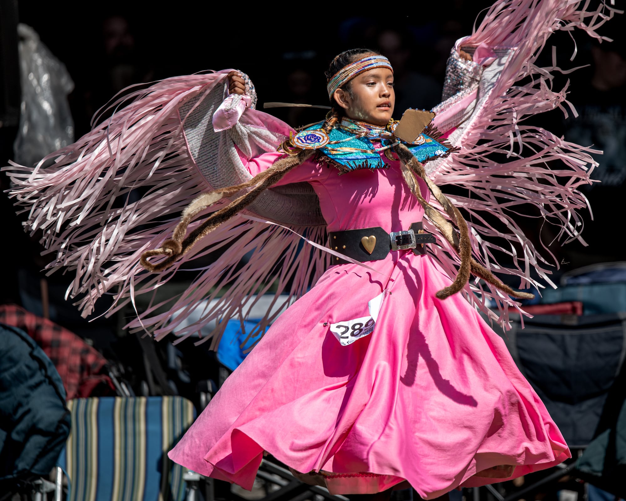 A young dancer raises her arms wearing pink regalia at 2025 Kamloopa powwow