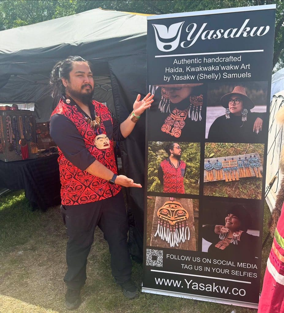 Robert Robinson of Nisga’a Nation poses with Yasakw Designs' booth banner 