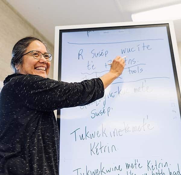 A teacher stands at a white board as she teacehes a class Secwepemctsín
