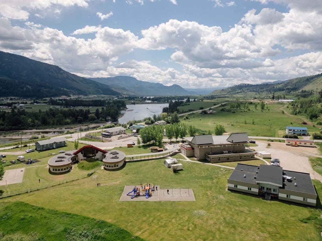 A cluster of school buildings are shown in a valley from up high showing blue sky with clouds
