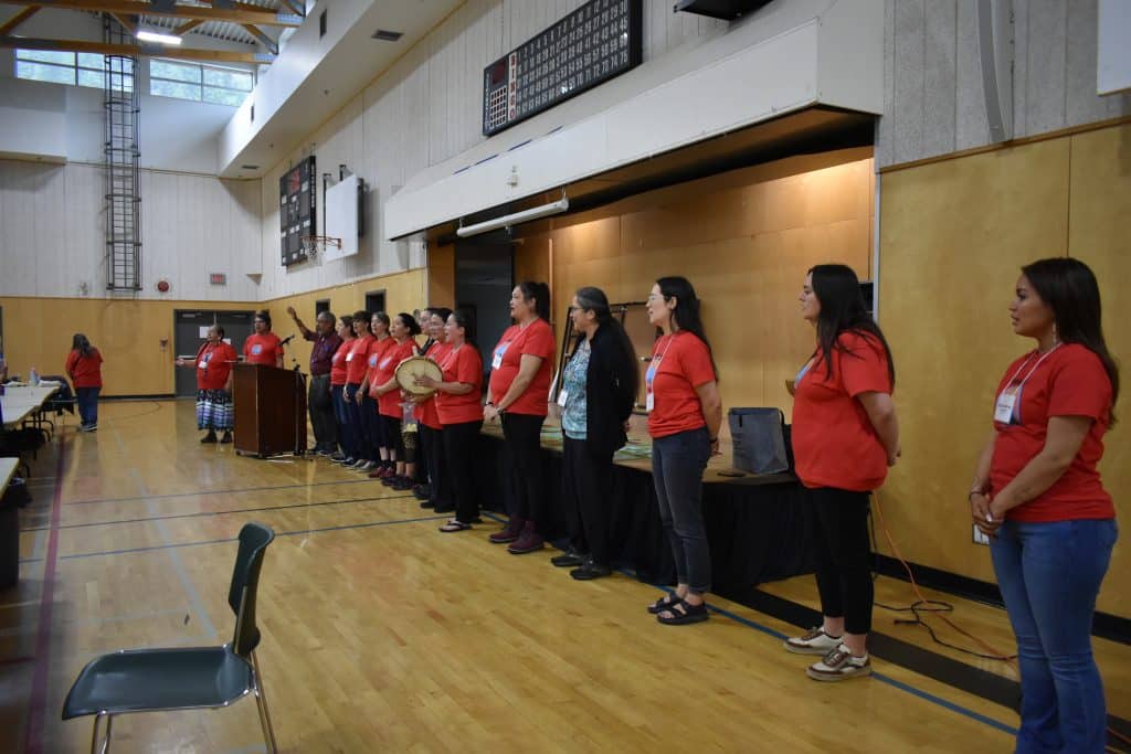 A row of educators stand for a song with drums in a gymnasium
