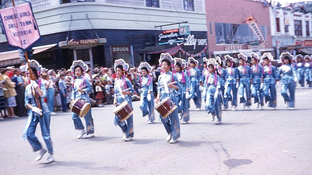 A Chinese-Canadian girls’ drill team from Victoria featuring drummers and marchers in bright blue silk costumes in the 1956 Kamloops Dominion Day parade