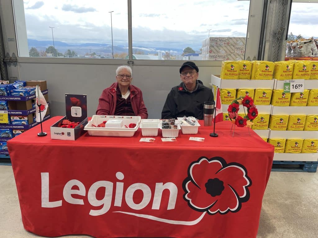 Two people sitting behind a table that has the Legion logo collecting funds for the poppy campaign ahead of Remembrance Day in Kamloops. 