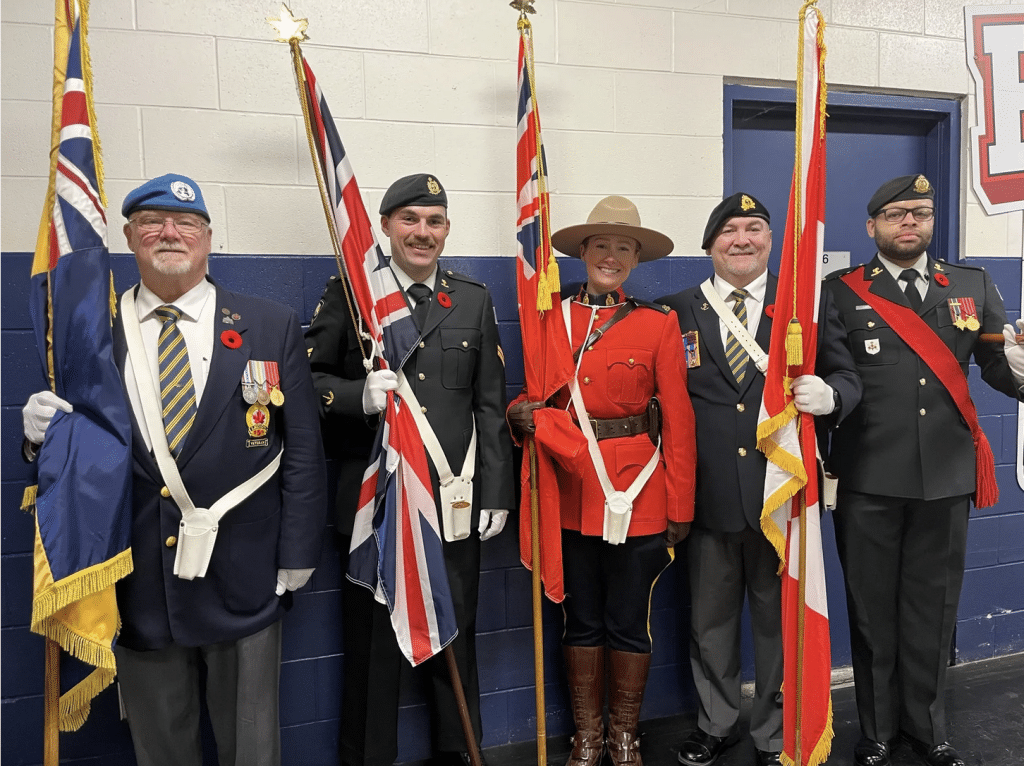 Five members of the legion with their uniforms and flags and red poppies. They participate in an event that seeks to highlight Remembrance Day. 