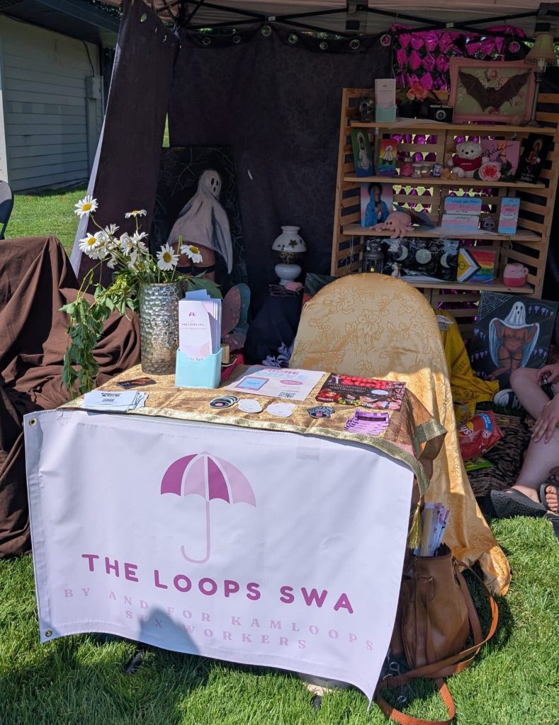 A table with the sign of The Loops SWA, on the table there are flyers, stickers and other information on the services offered by the organization to sex workers.