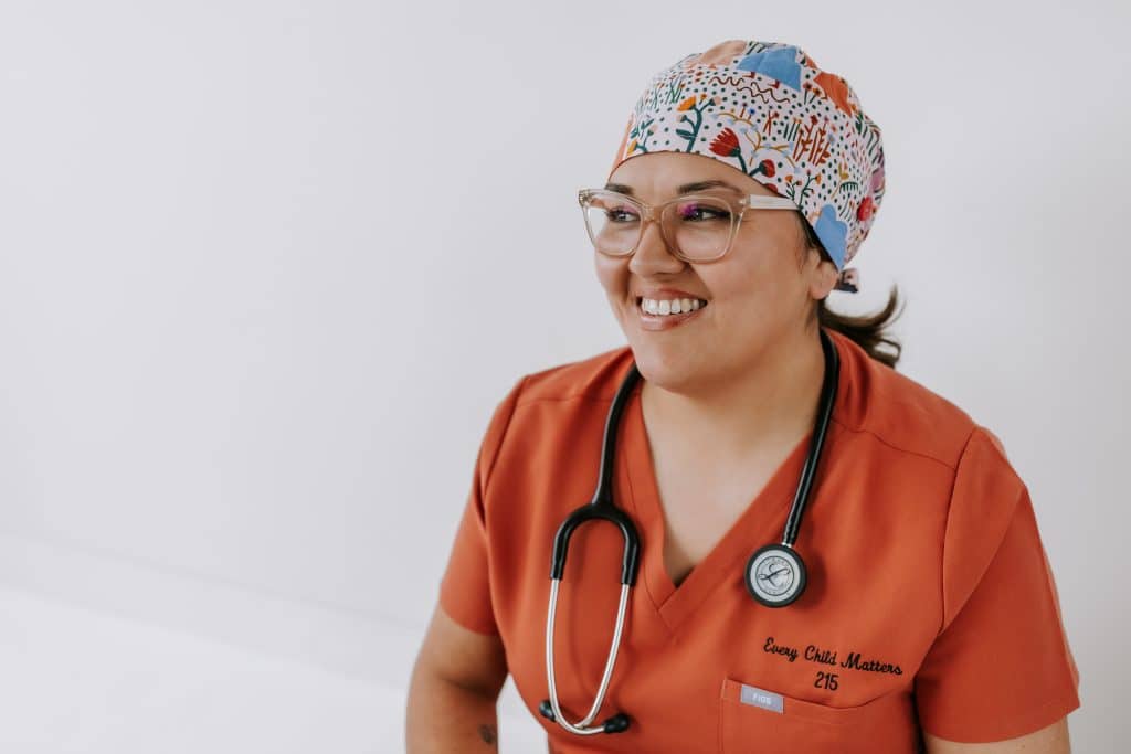 A woman smiles for a photo wearing scrubs and a headband in preparation for labour.