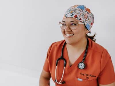 A woman smiles for a photo wearing scrubs and a headband in preparation for labour.