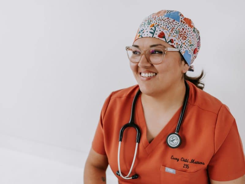A woman smiles for a photo wearing scrubs and a headband in preparation for labour.