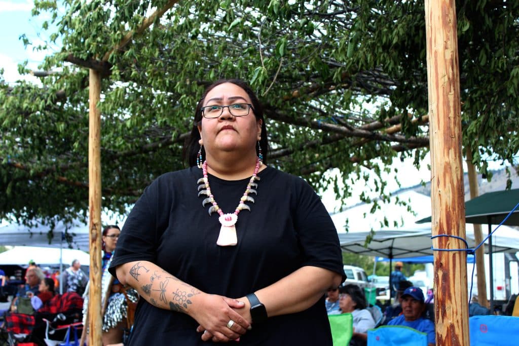 A woman in a black shirt wearing a large necklace stands in reflection during a speech