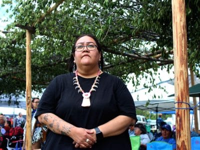 A woman in a black shirt wearing a large necklace stands in reflection during a speech