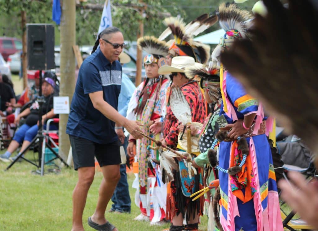 A man shakes hands with dancers in regalia outside